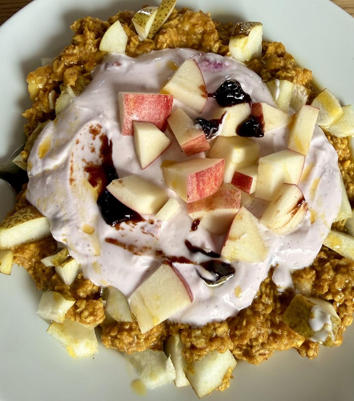 Amber Morning Bowl: goldenes Kurkuma-Porridge mit zart lila Proteincreme, Apfel- und Birnenwürfeln, dunklen Pflaumenmus-Tupfen und Honigfaden auf weißem Teller