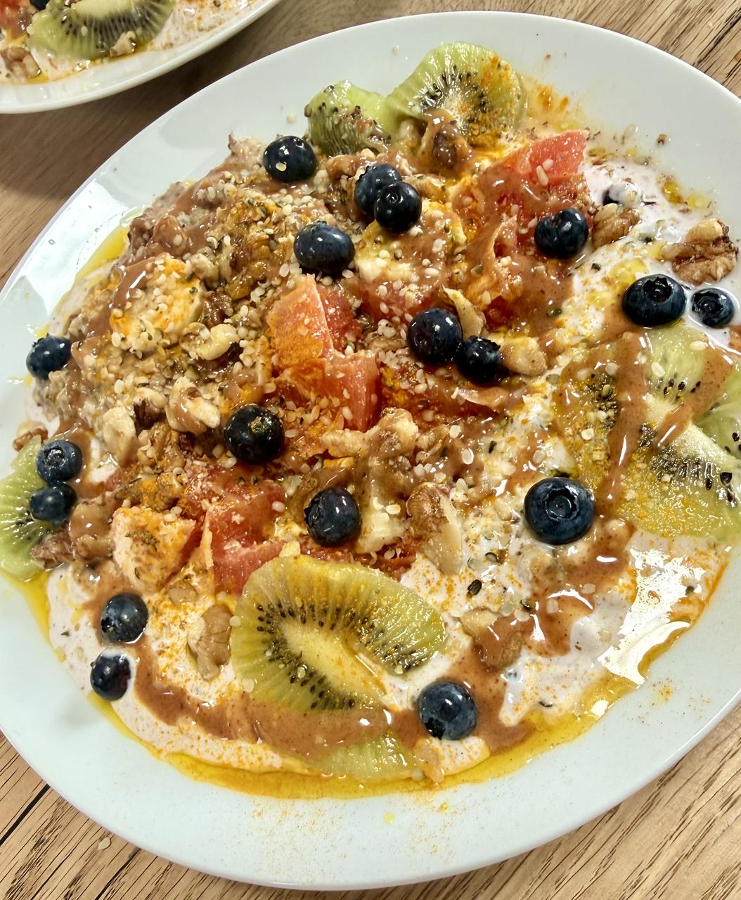Golden Grapefruit Bowl: Grapefruit-Segmente, Kiwischeiben und frische Heidelbeeren auf heller Proteincreme mit Kurkuma-Gold und Mandelmus-Drizzle, als flacher Teller angerichtet
