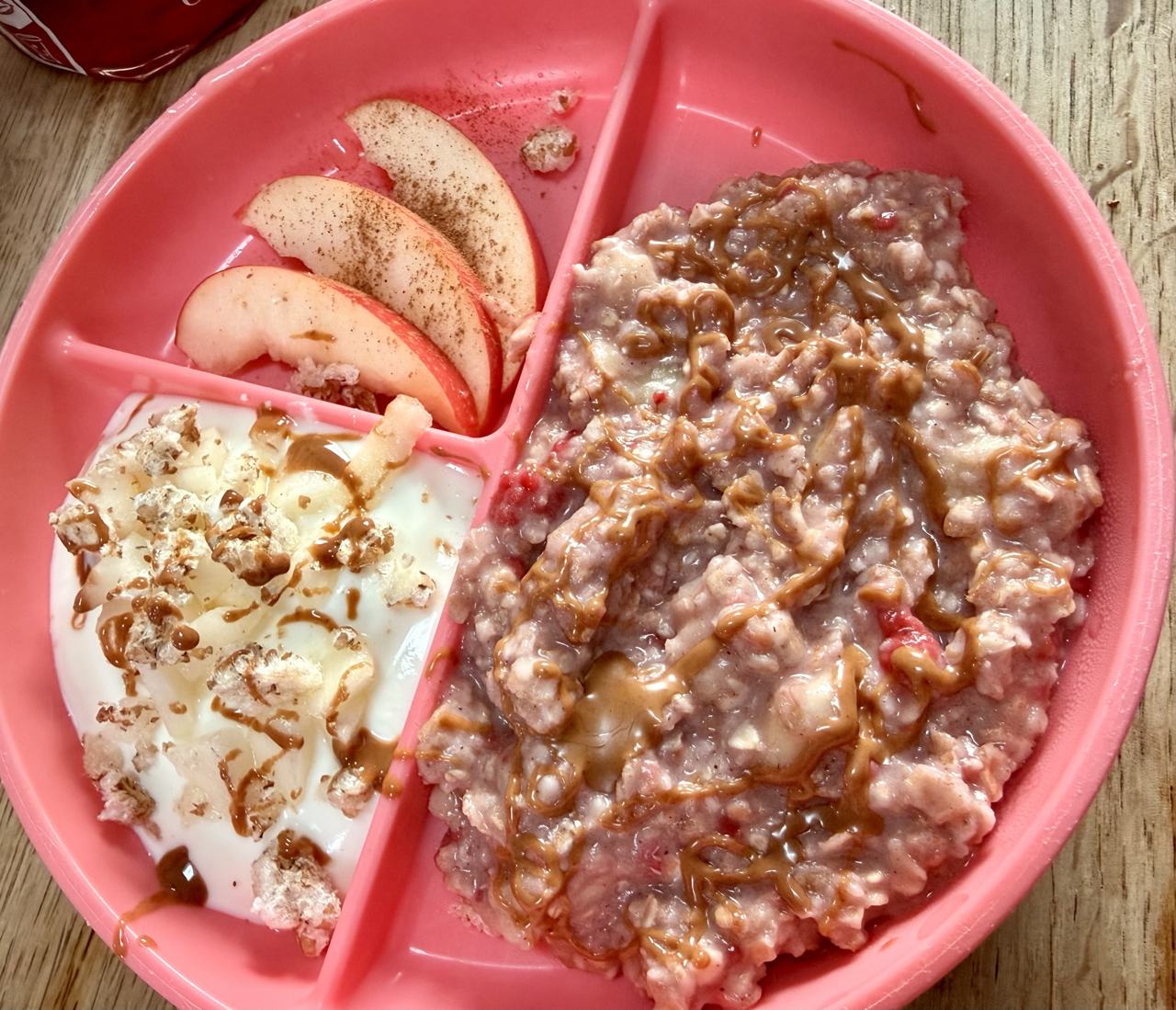 Kleini Berry Bowl: rosa Kinderteller mit drei Fächern – warmes rosa Beeren-Porridge mit Mandelmus-Drizzle im großen Fach, daneben Joghurt-Dip mit Birnenwürfeln und Dinkel-Pops sowie dünne Apfelspalten mit Zimt