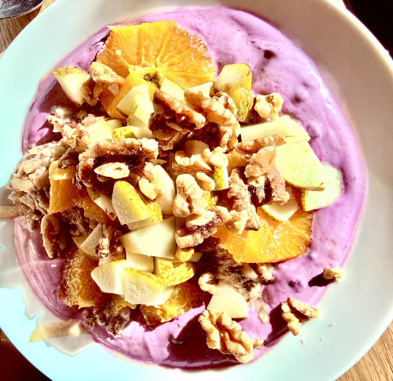 Purple Sunrise Bowl: lila Heidelbeer-Creme mit Orangenscheiben, Birnenwürfeln und Walnüssen in heller Schale