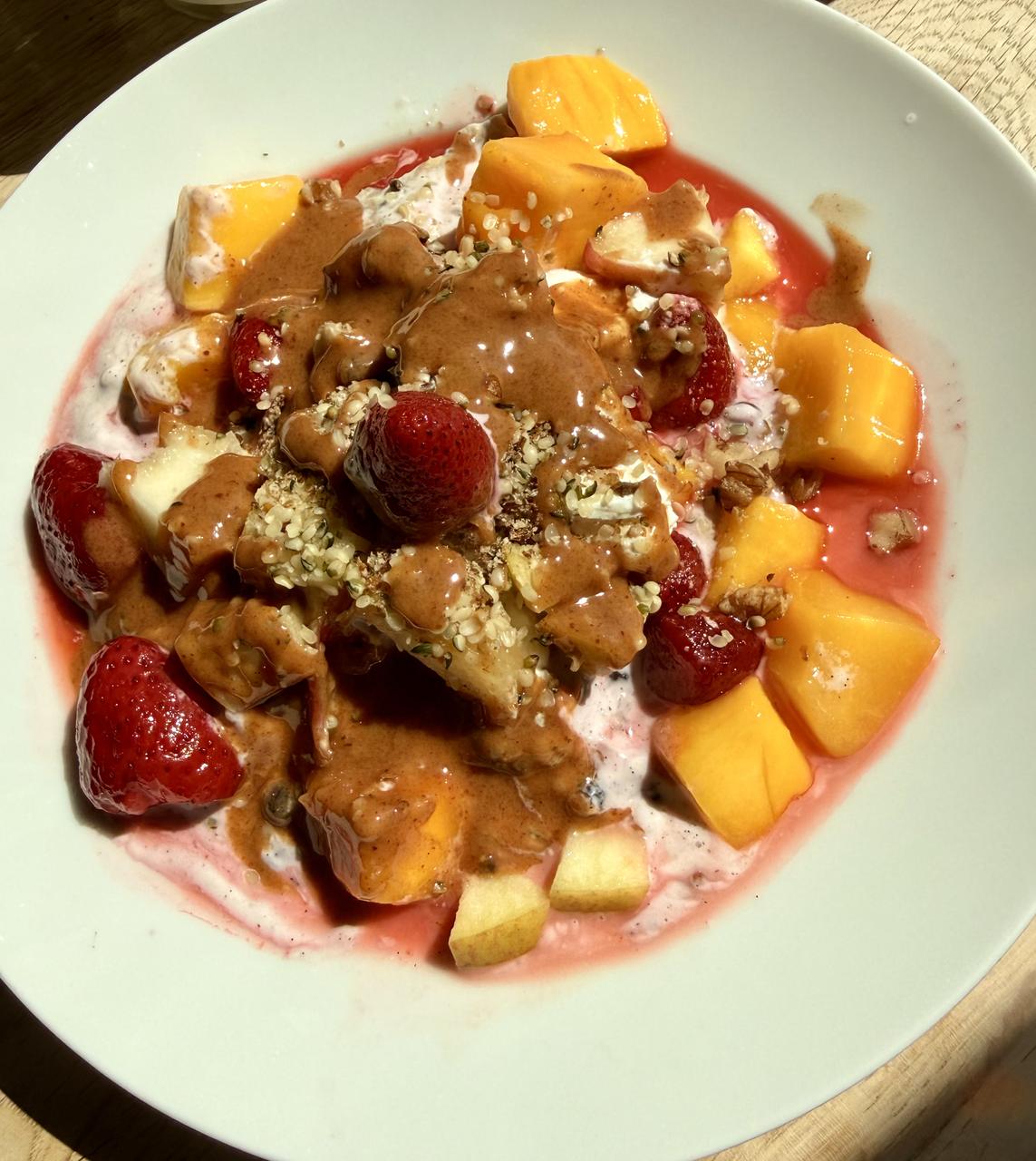 Ruby Mango Bowl: TK-Erdbeeren samt rotem Saft und Mangowürfel auf lila Heidelbeer-Creme, mit Apfel, Hanfsamen, Walnüssen und Amlou-Faden